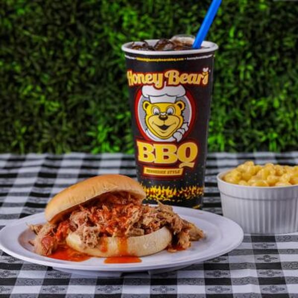 Honey Bear's BBQ pulled pork sandwich, mac and cheese, and branded drink on a checkered tablecloth.
